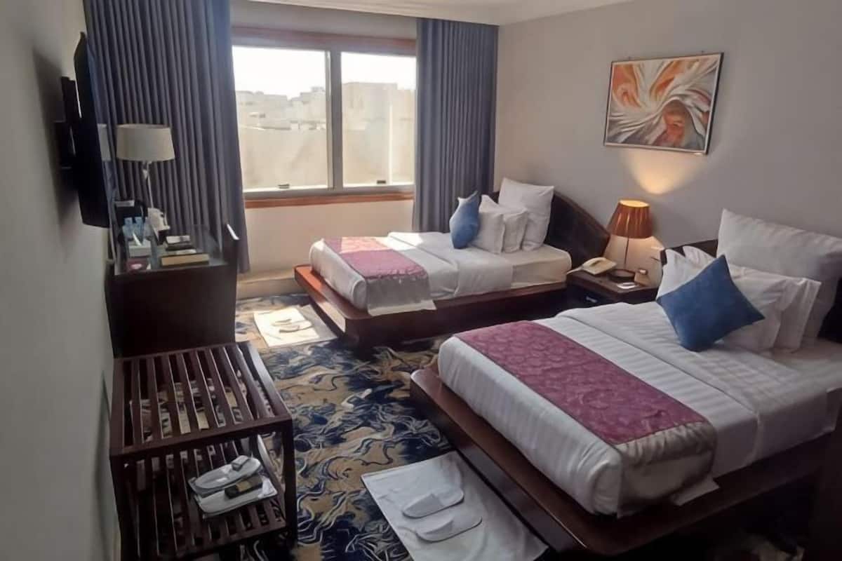 A hotel room with two beds, a desk, a TV, and a window with curtains.