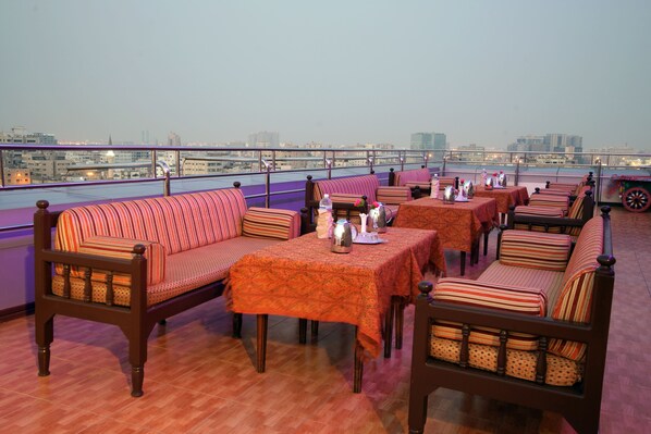 A rooftop restaurant with seating arrangements, tables, and a view of the cityscape.