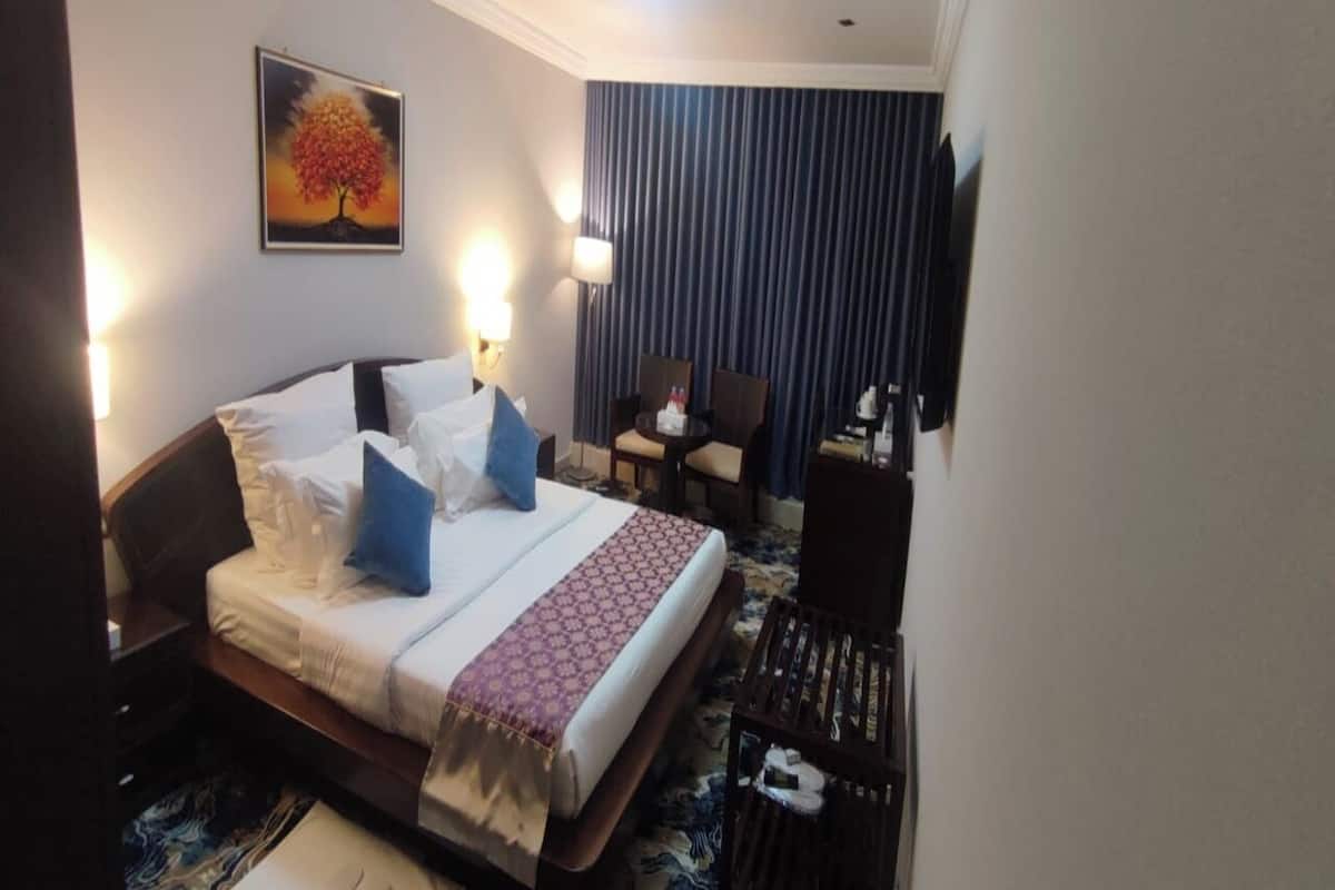 A hotel room with a bed, bedside tables, a desk, a chair, a lamp, and a painting on the wall.