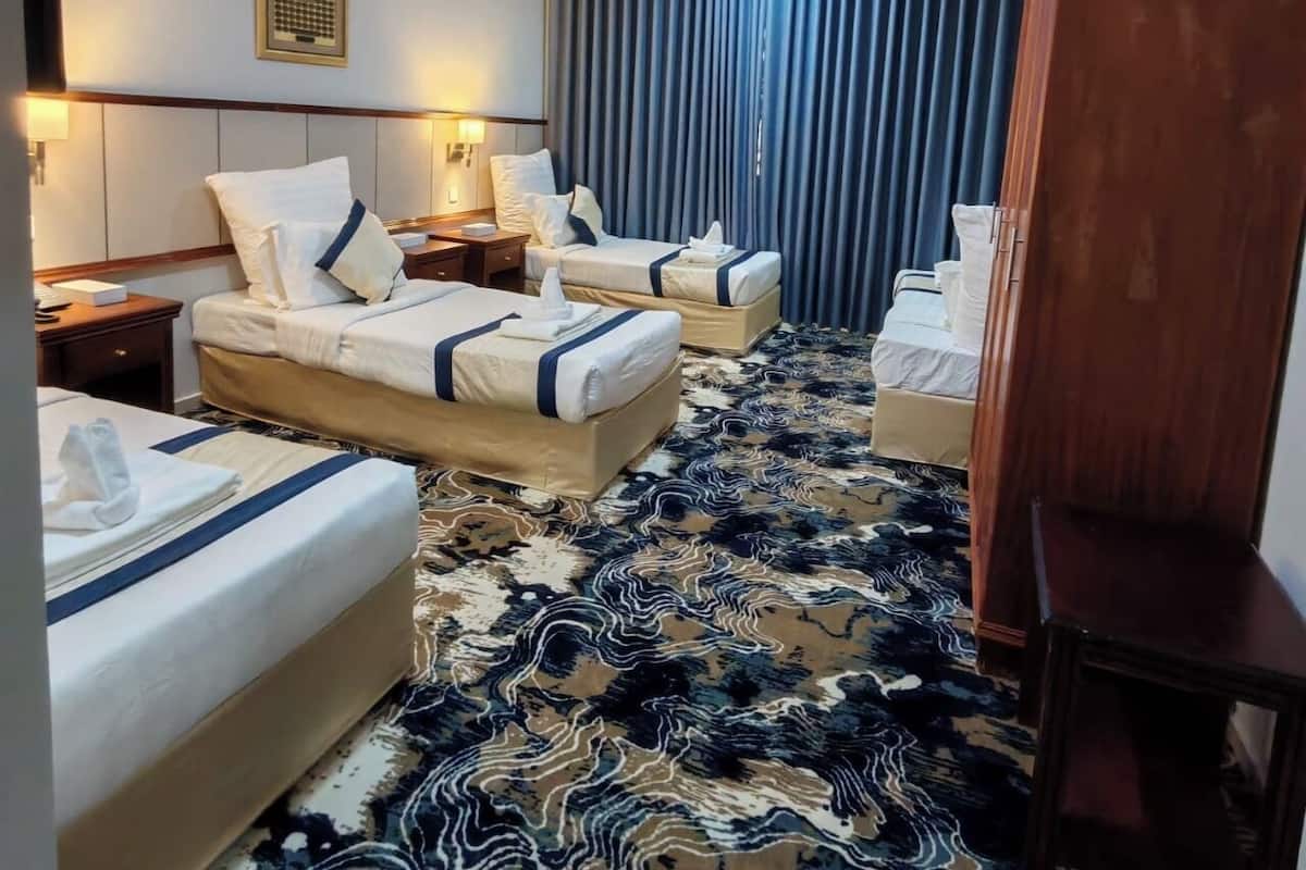 A hotel room with two beds, a large window with blue curtains, a patterned carpet, and a wooden wardrobe.