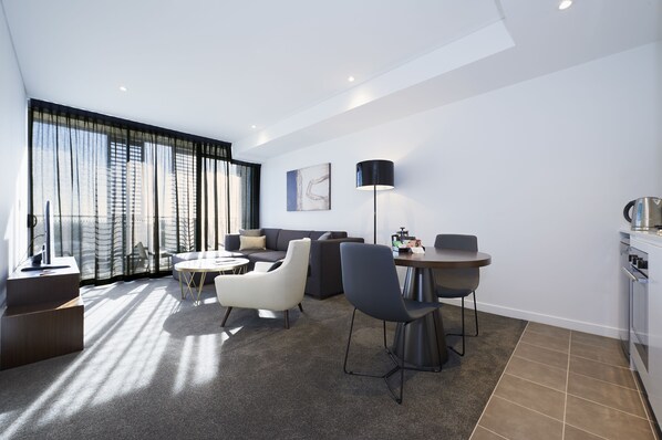 Una habitación de hotel moderna con sofá, sillas, mesa de comedor y zona de cocina.