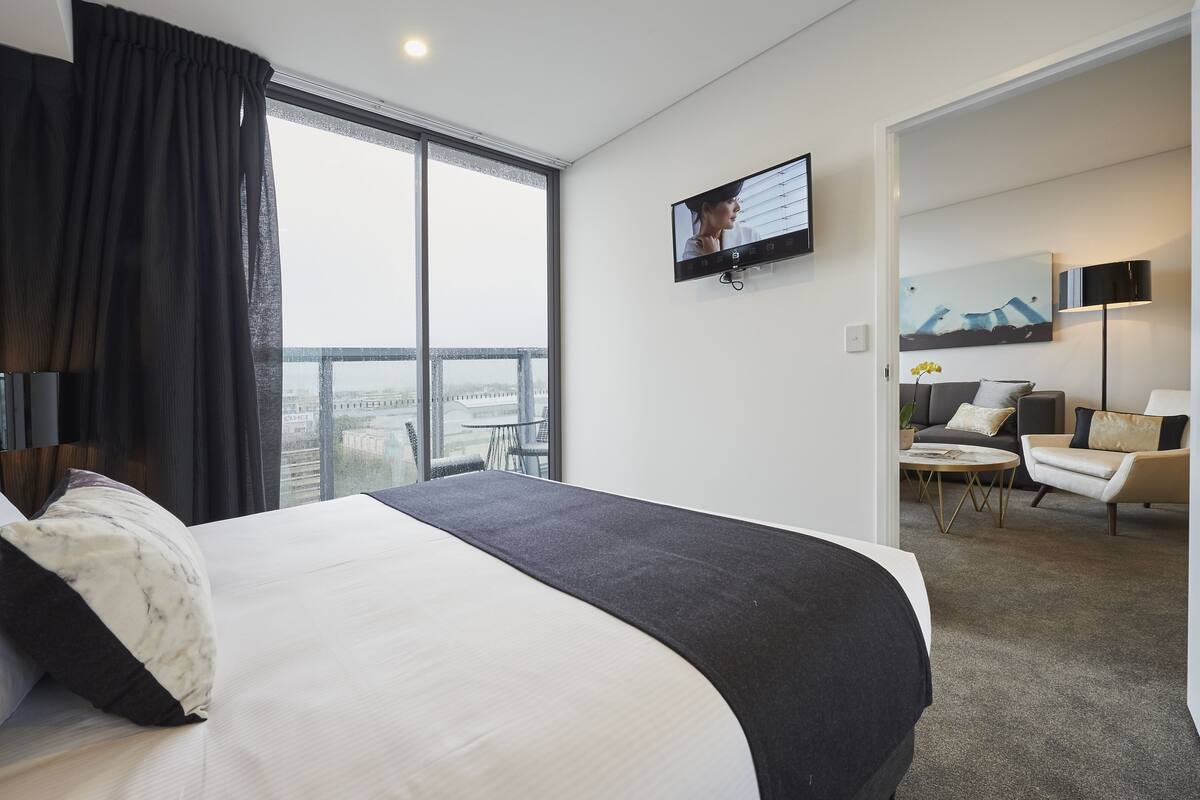A modern hotel room with a large bed, a TV mounted on the wall, a sofa, and a small table.