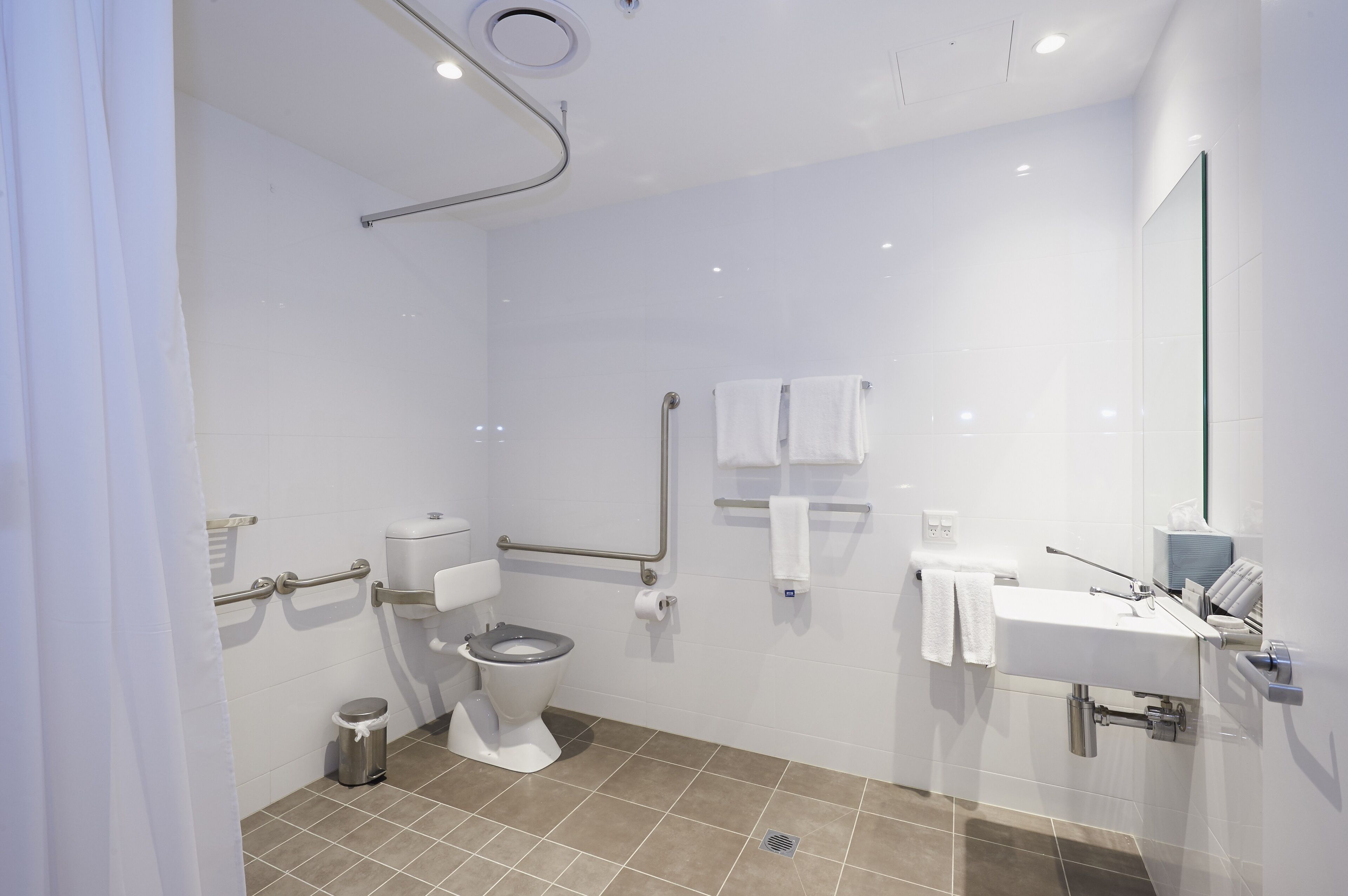 A modern bathroom with a toilet, bidet, and sink, equipped with grab bars and a hand dryer.