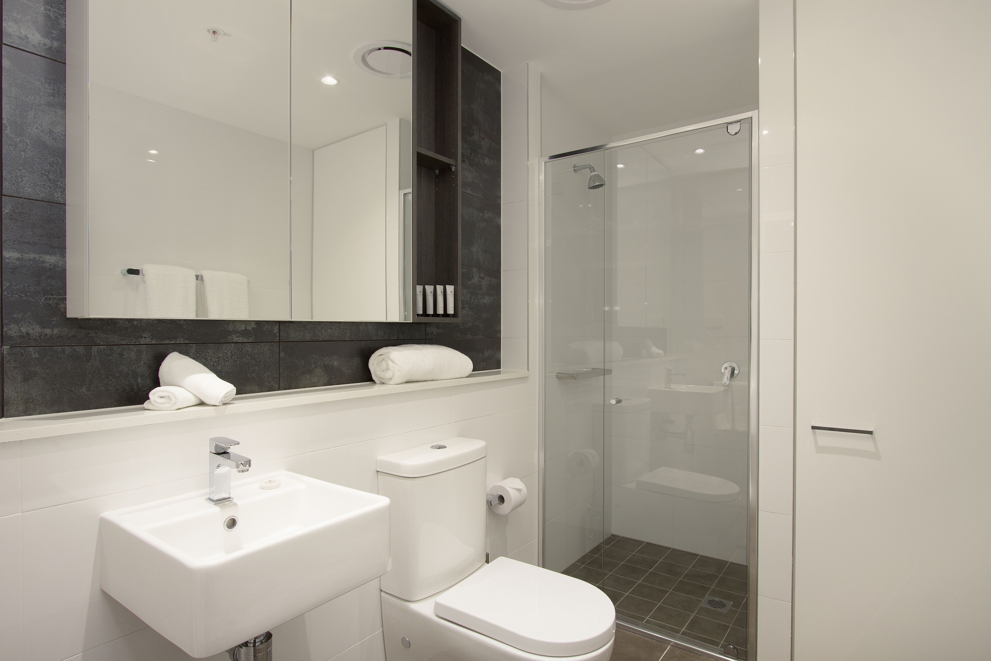 A modern bathroom with a white sink, toilet, and glass-enclosed shower.