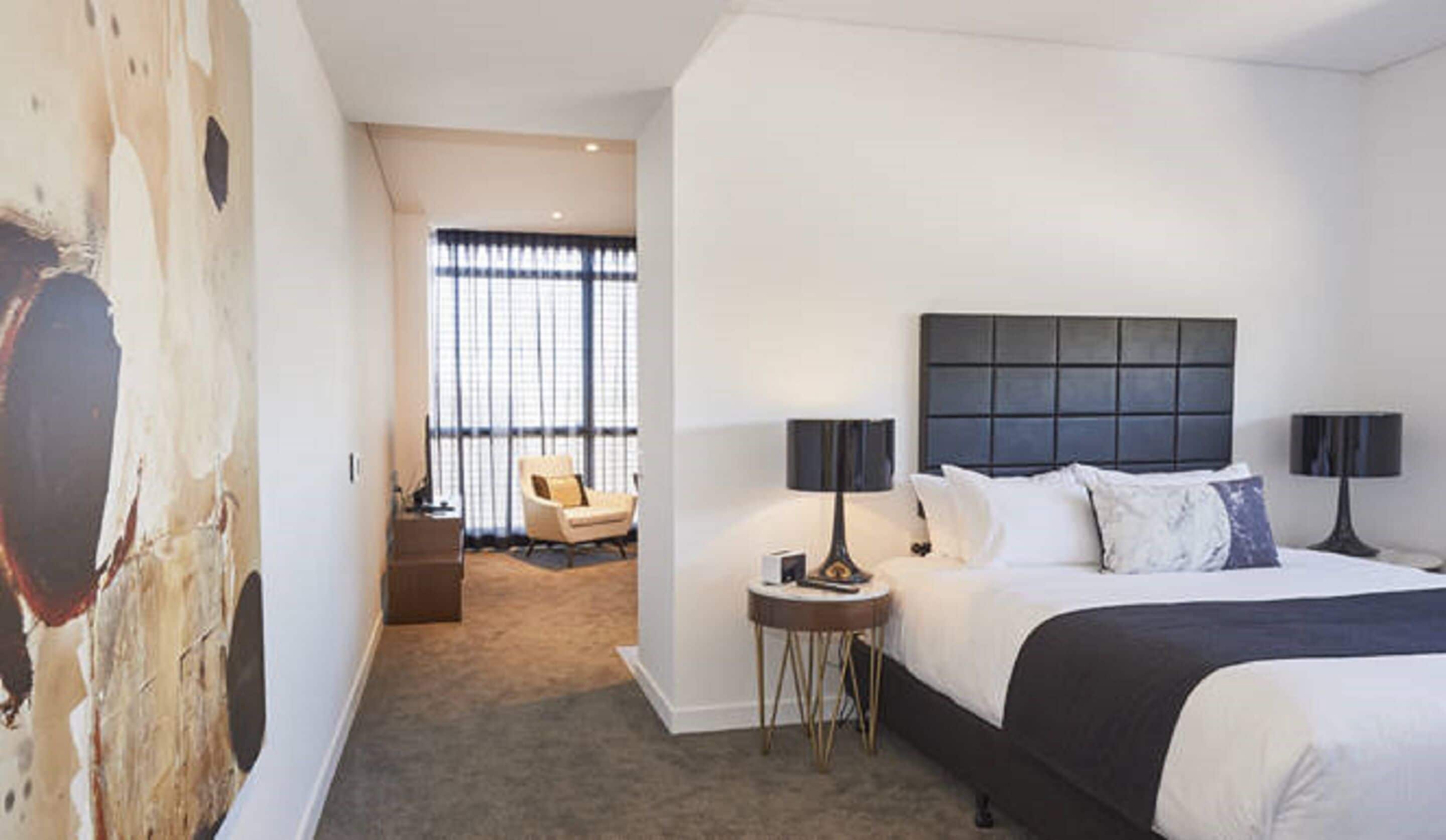 Ett modernt hotellrum med en stor säng, två sängbord, en stol och utsikt genom ett stort fönster.