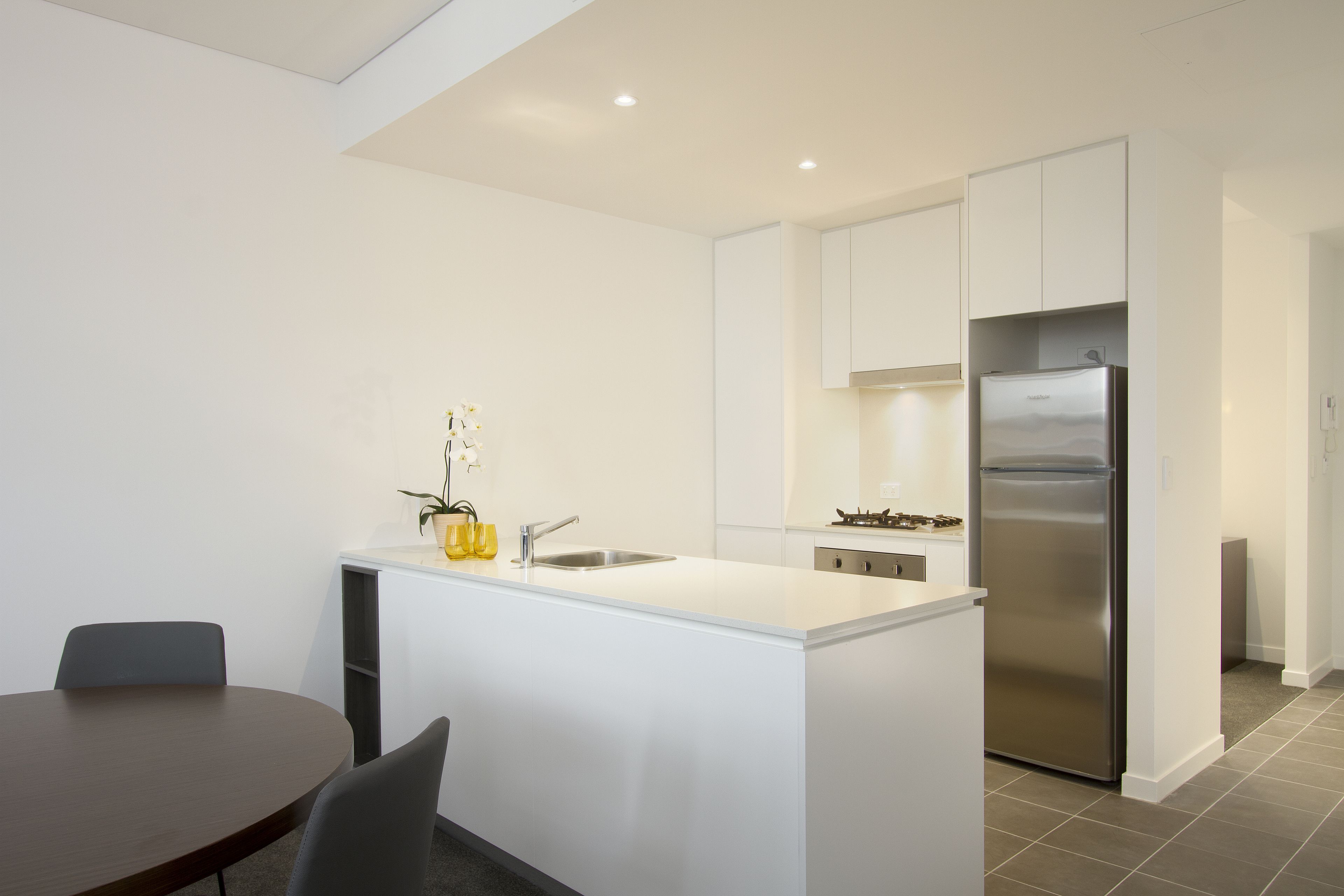 A modern kitchen with white cabinetry, a stainless steel refrigerator, and a central island with a sink.