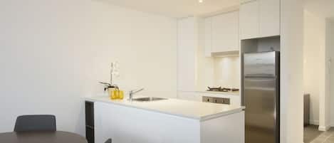 A modern kitchen with white cabinetry, a stainless steel refrigerator, and a central island with a sink.