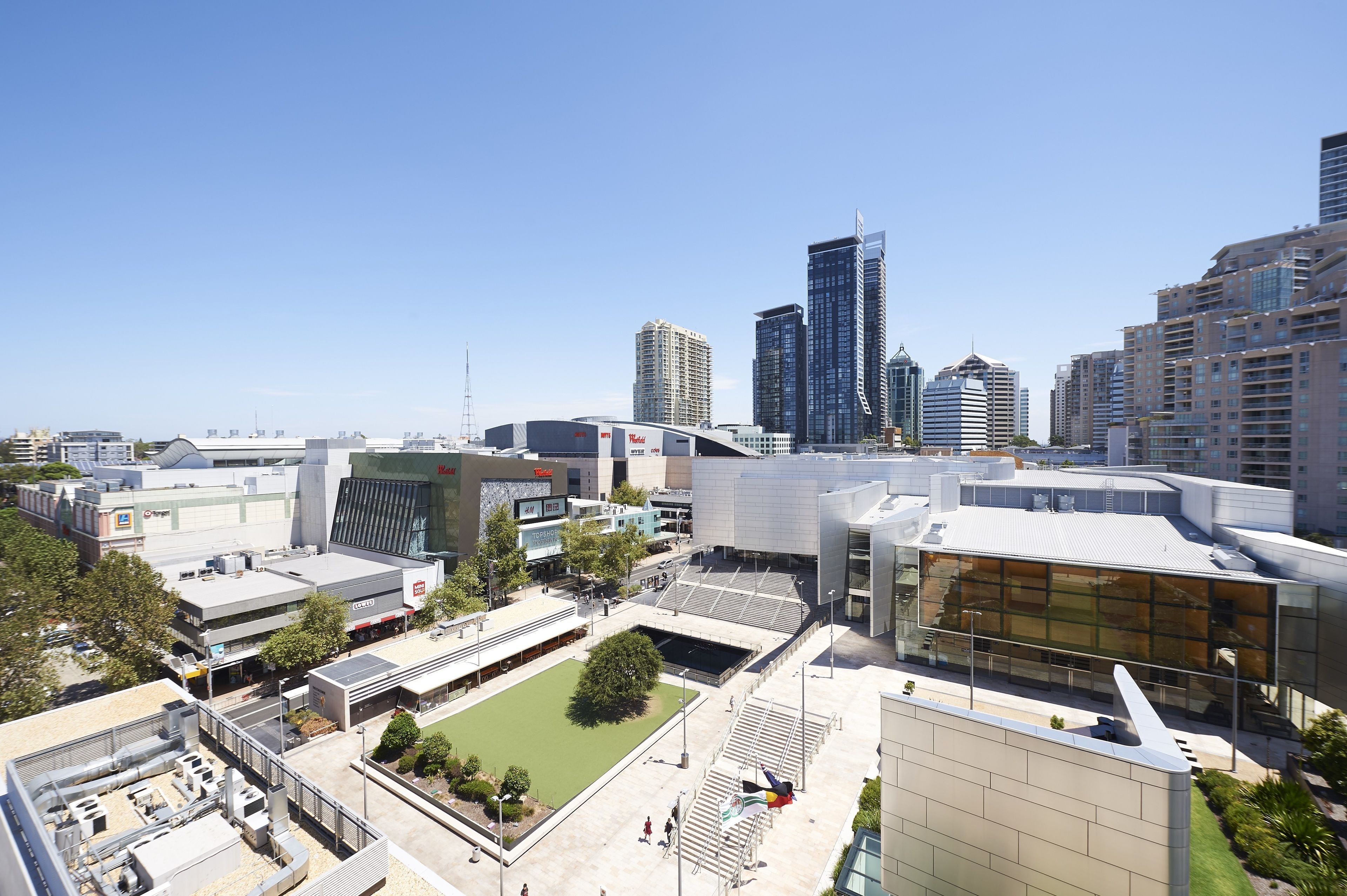 A modern urban area with high-rise buildings, a large glass structure, and a green space.