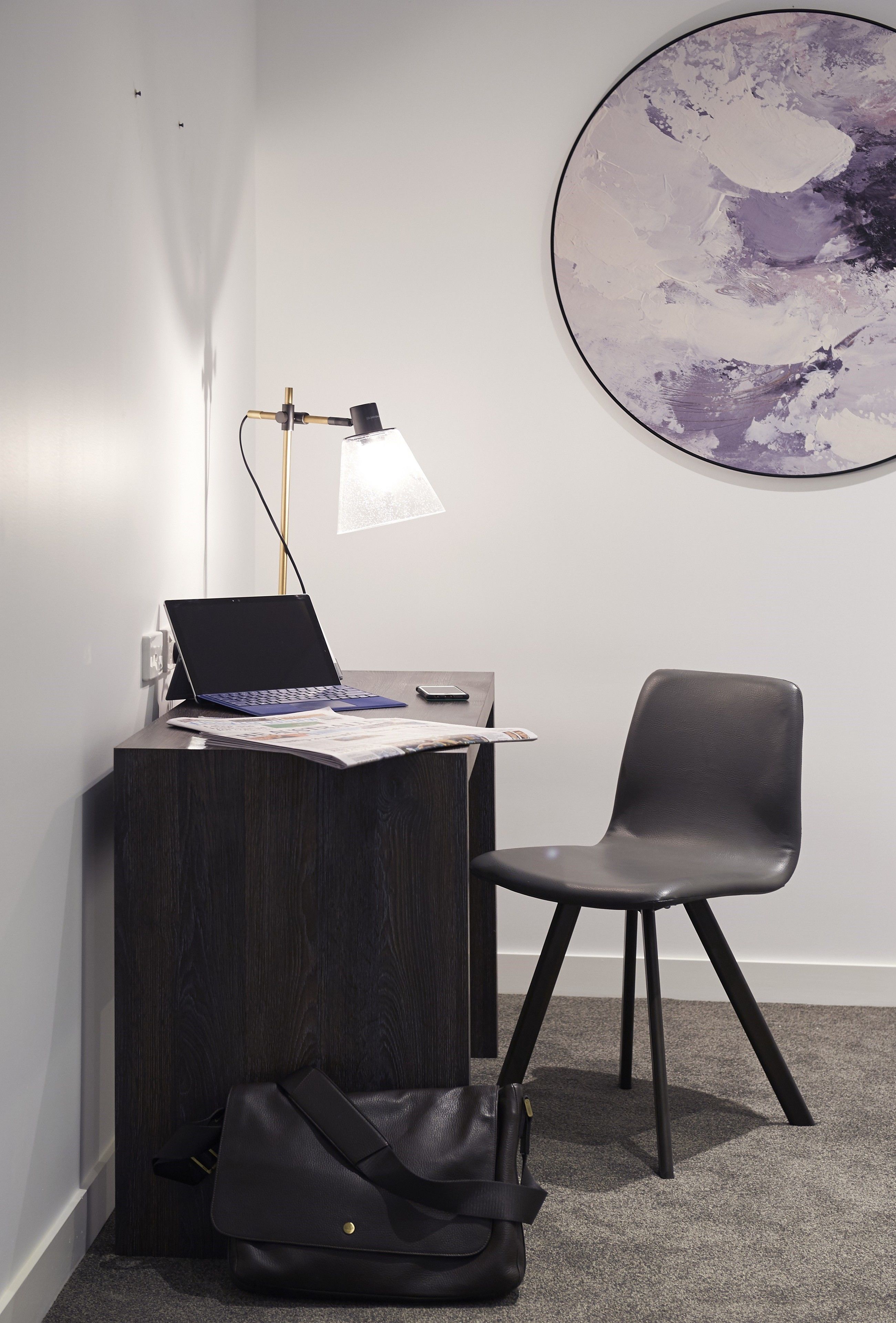 A modern office space with a desk, laptop, lamp, chair, and a large abstract painting on the wall.