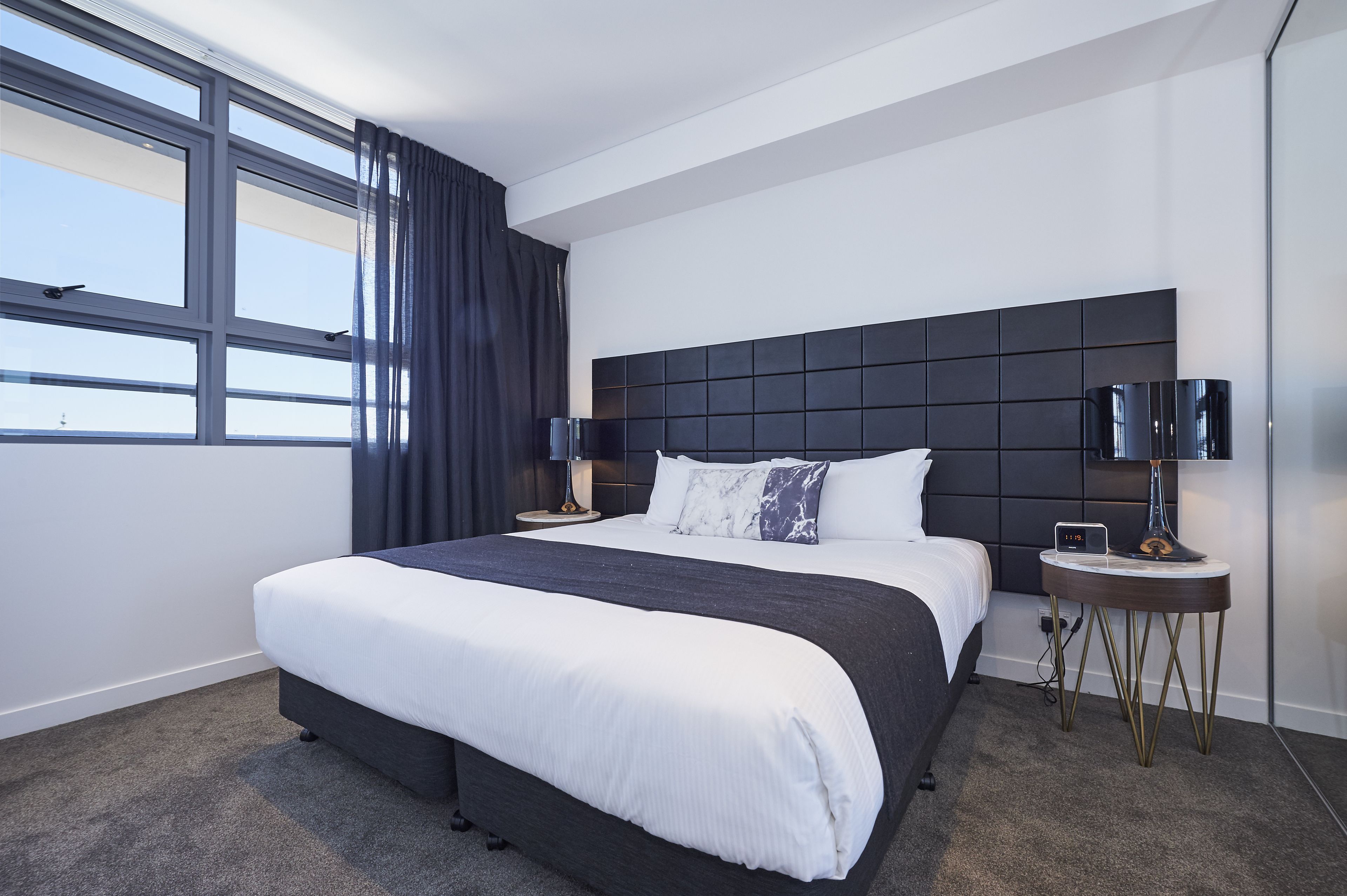 Ein modernes Hotelzimmer mit einem großen Bett, einer dunklen Kopfteil und zwei Nachttischen mit Lampen.