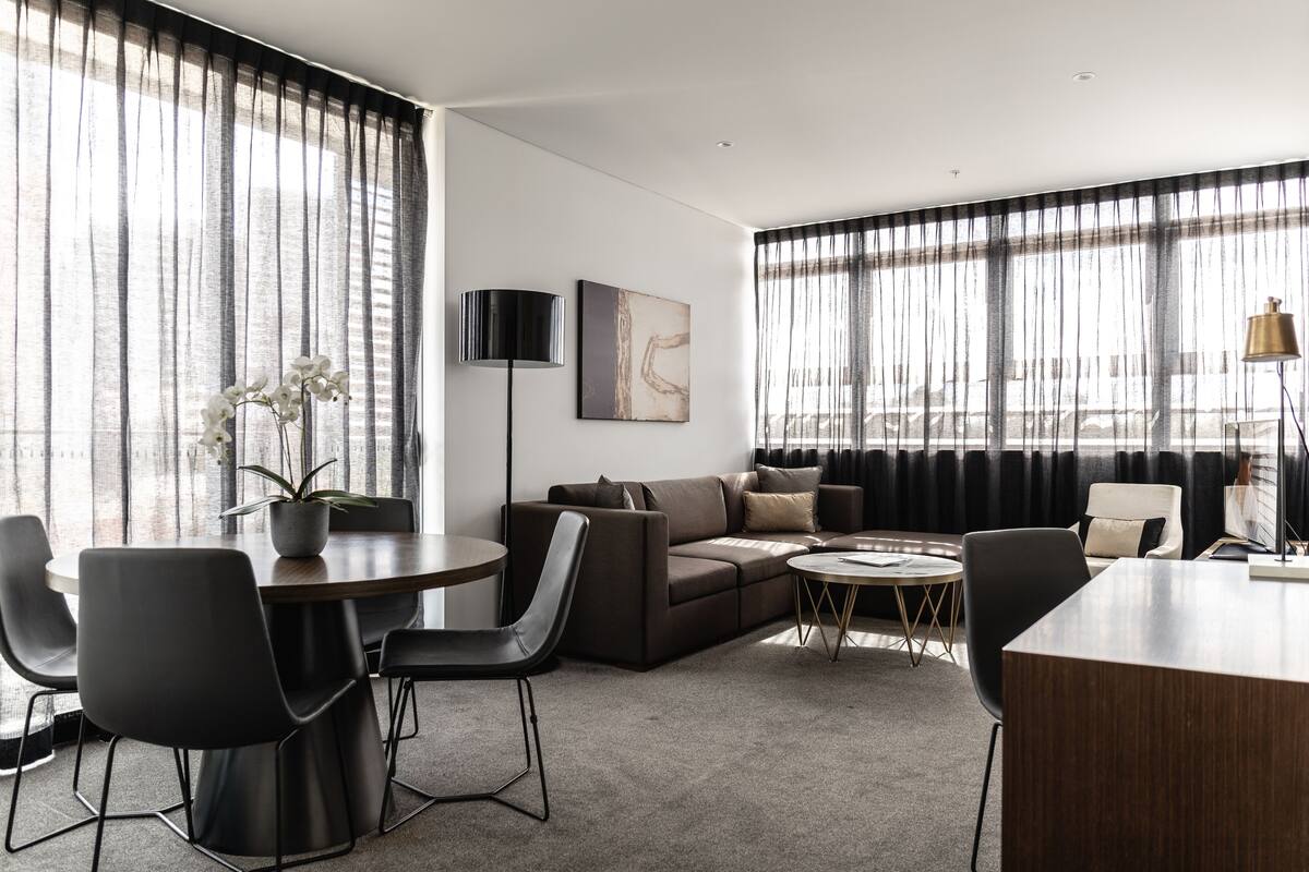 A modern living room with a sofa, chairs, a dining table, and a coffee table. There is a potted plant on the table and a painting on the wall.