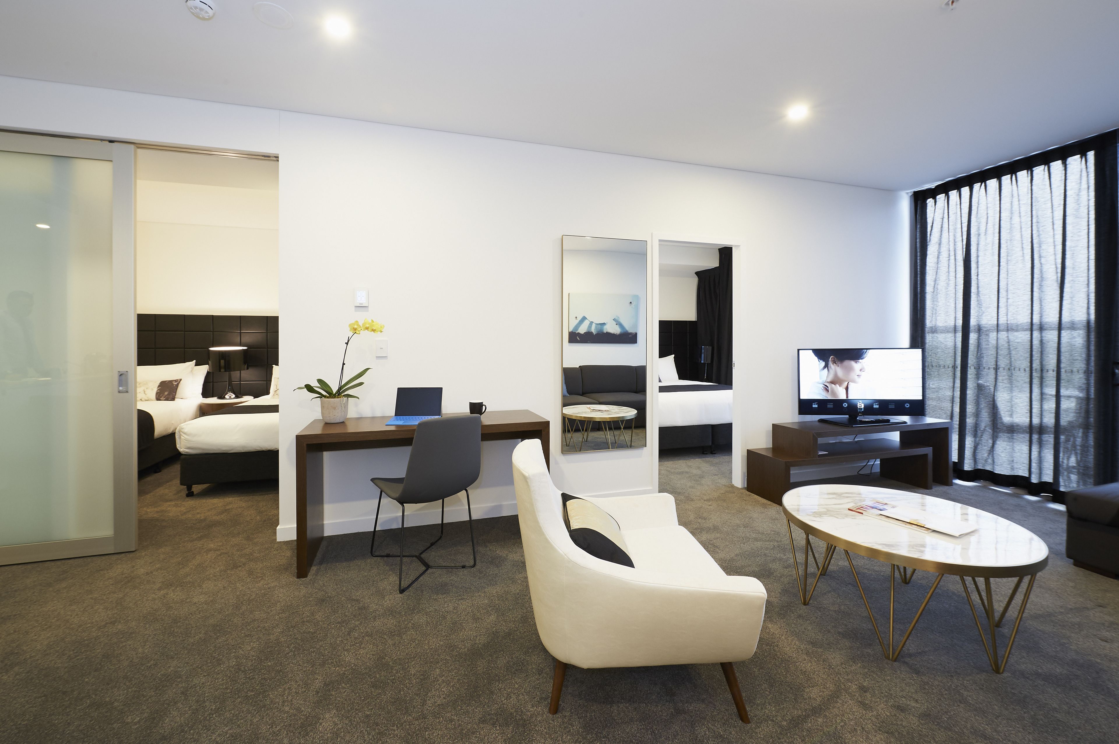 Una habitación de hotel moderna con cama, escritorio, silla, sofá, televisión y ventanas amplias.