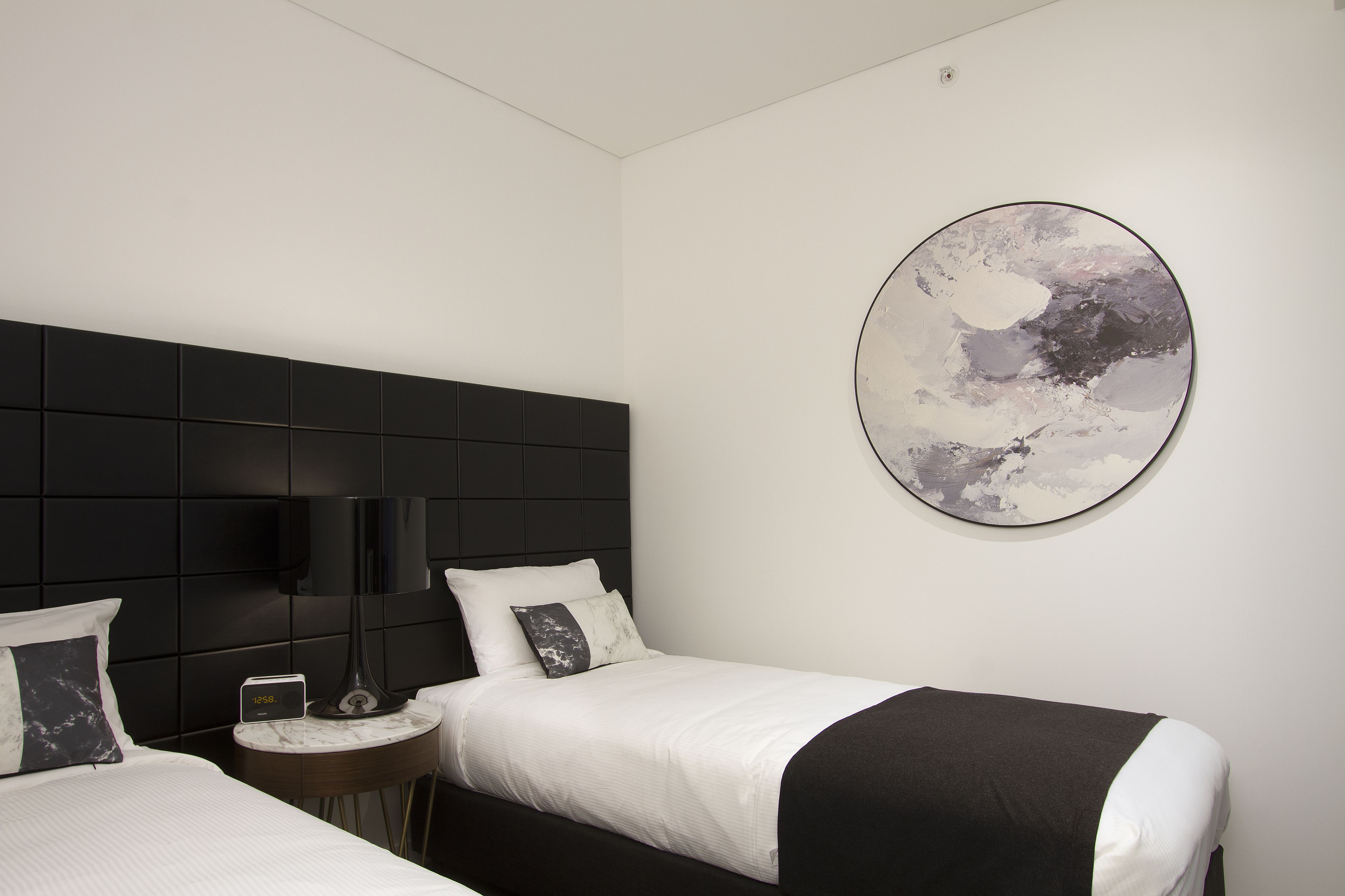 Ein modernes Hotelzimmer mit zwei Betten, einem runden, abstrakten Gemälde und einem Nachttisch mit Lampe.