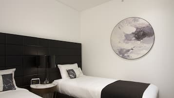 Ein modernes Hotelzimmer mit zwei Betten, einem runden, abstrakten Gemälde und einem Nachttisch mit Lampe.
