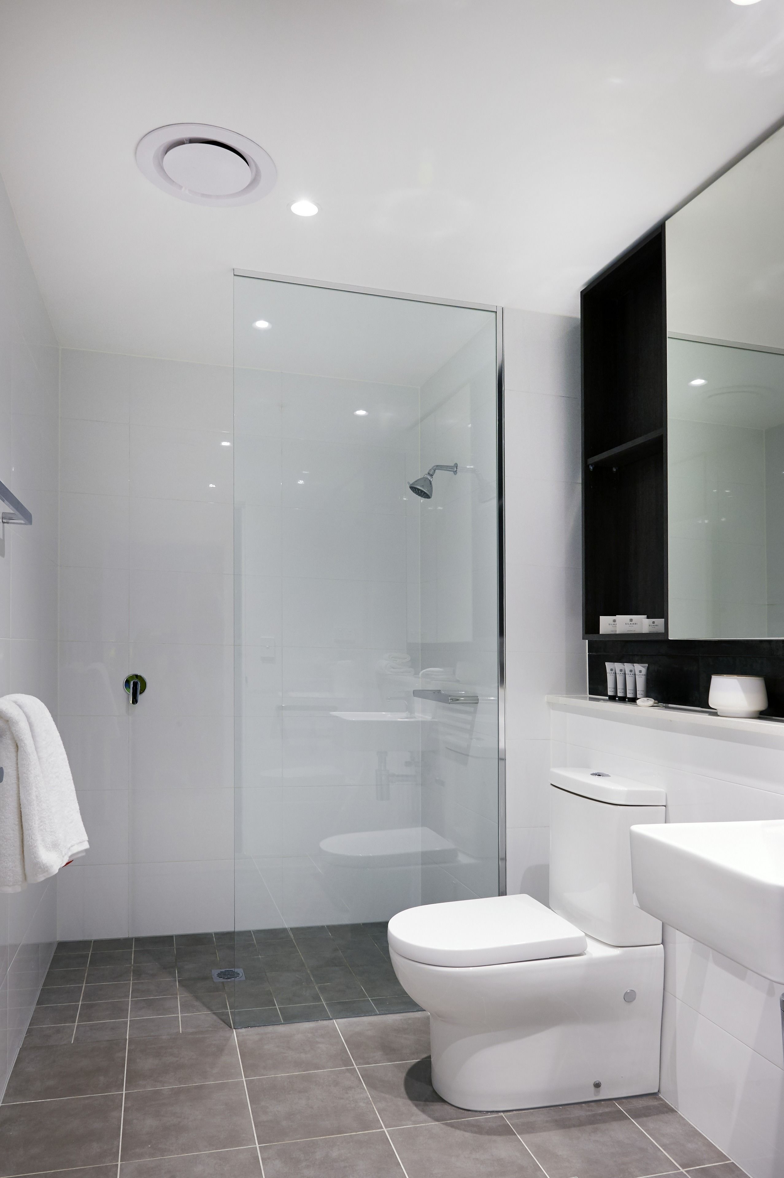 Un baño moderno con cabina de ducha de vidrio, inodoro blanco y tocador con espejo.