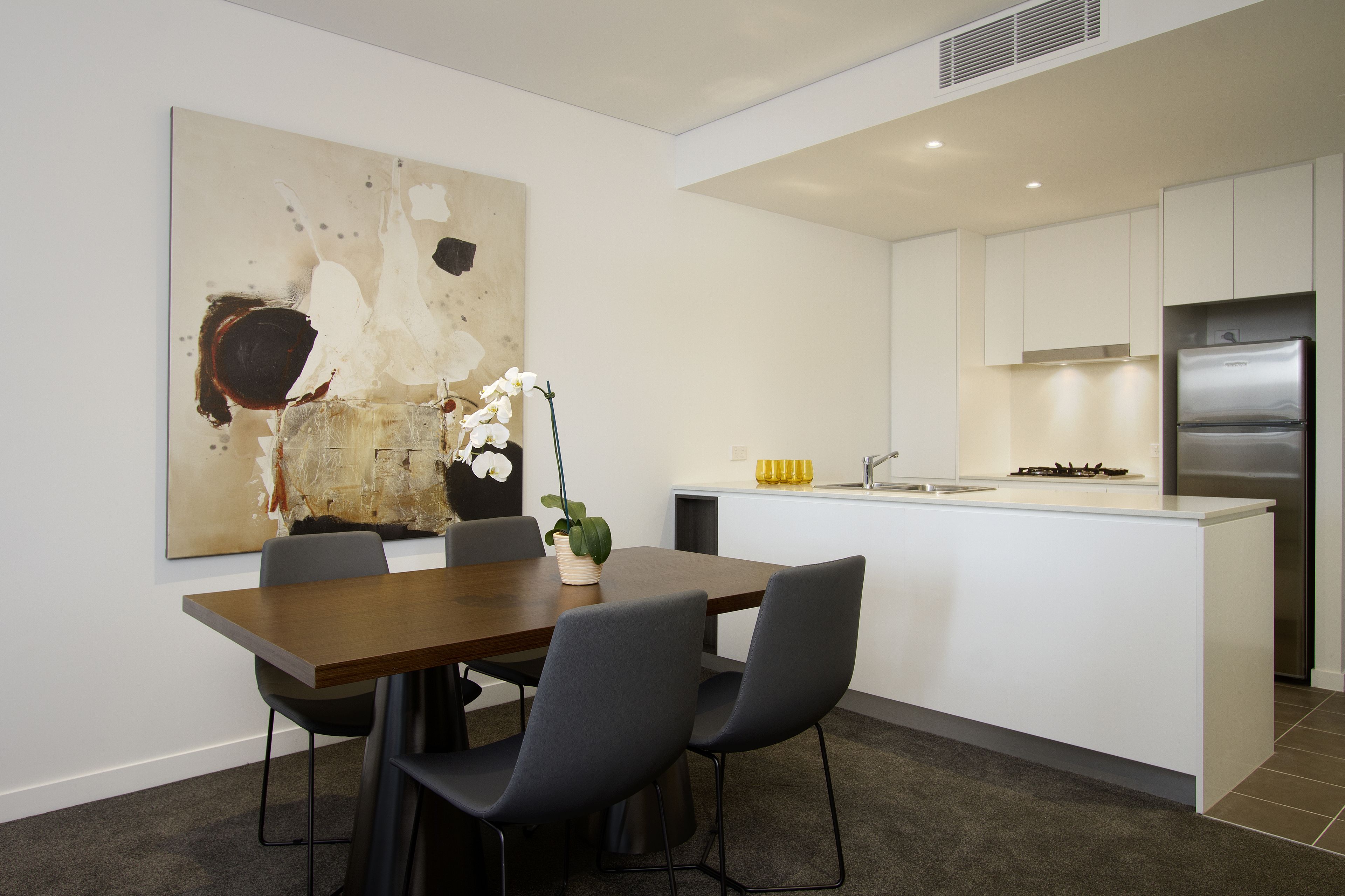 A modern kitchen with white cabinets, a stainless steel refrigerator, and a dining area with a wooden table and black chairs.