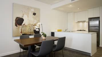 Eine moderne Küche mit weißen Schränken, einem Edelstahlkühlschrank und einem Essbereich mit einem Holztisch und schwarzen Stühlen.