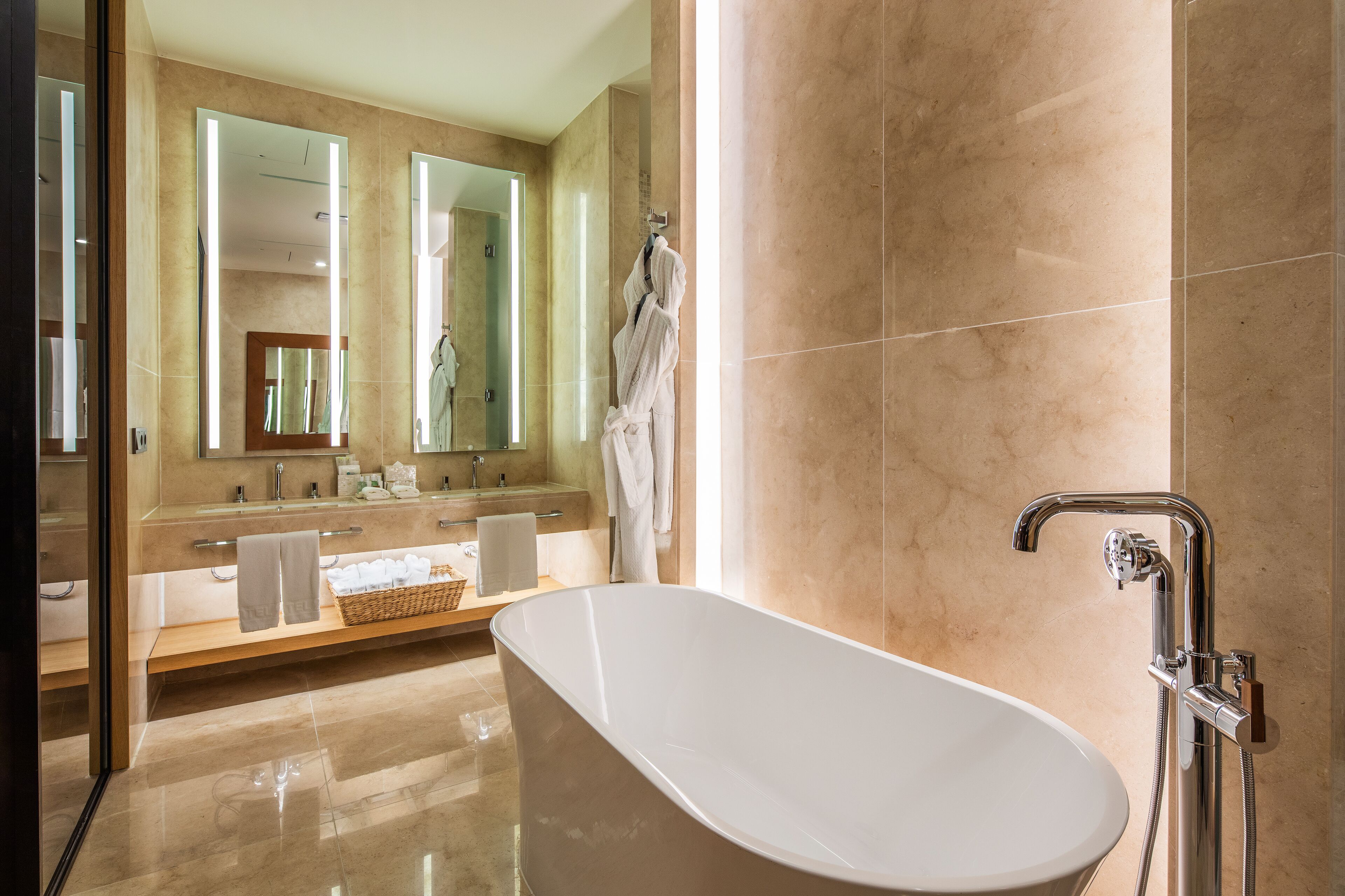 Un baño moderno con una bañera independiente, un espejo grande y un tocador con lavabo y toallero.
