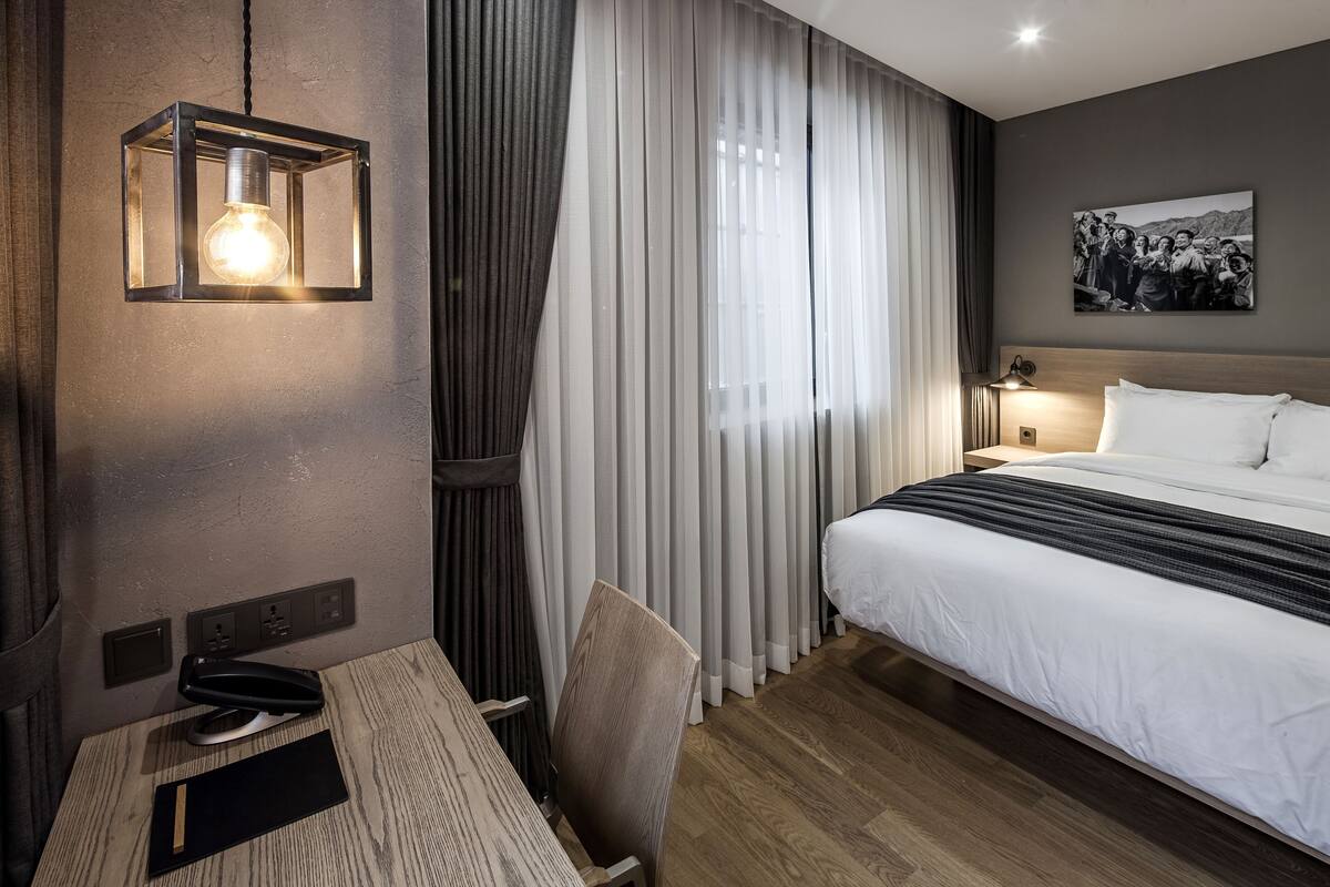 A hotel room with a bed, a desk, a chair, a lamp, and a picture on the wall.