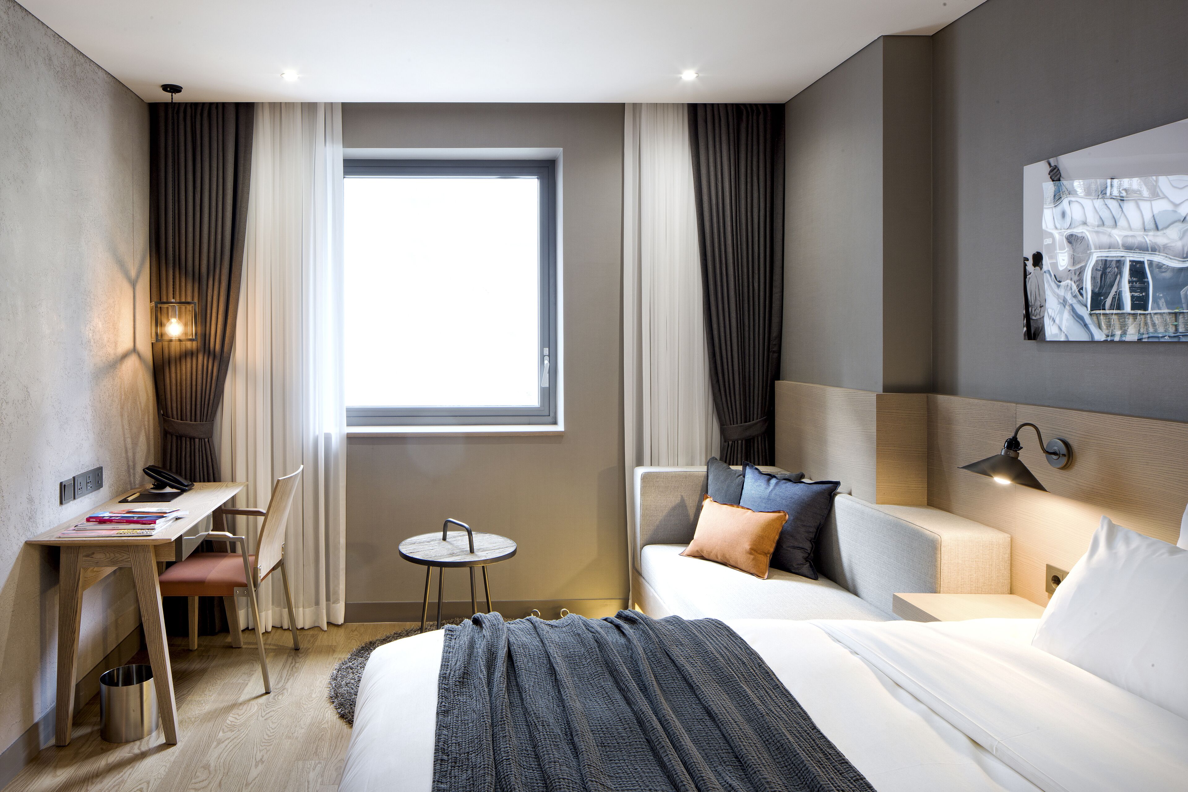 Una habitación de hotel moderna con cama, escritorio, silla y una pequeña mesa.
