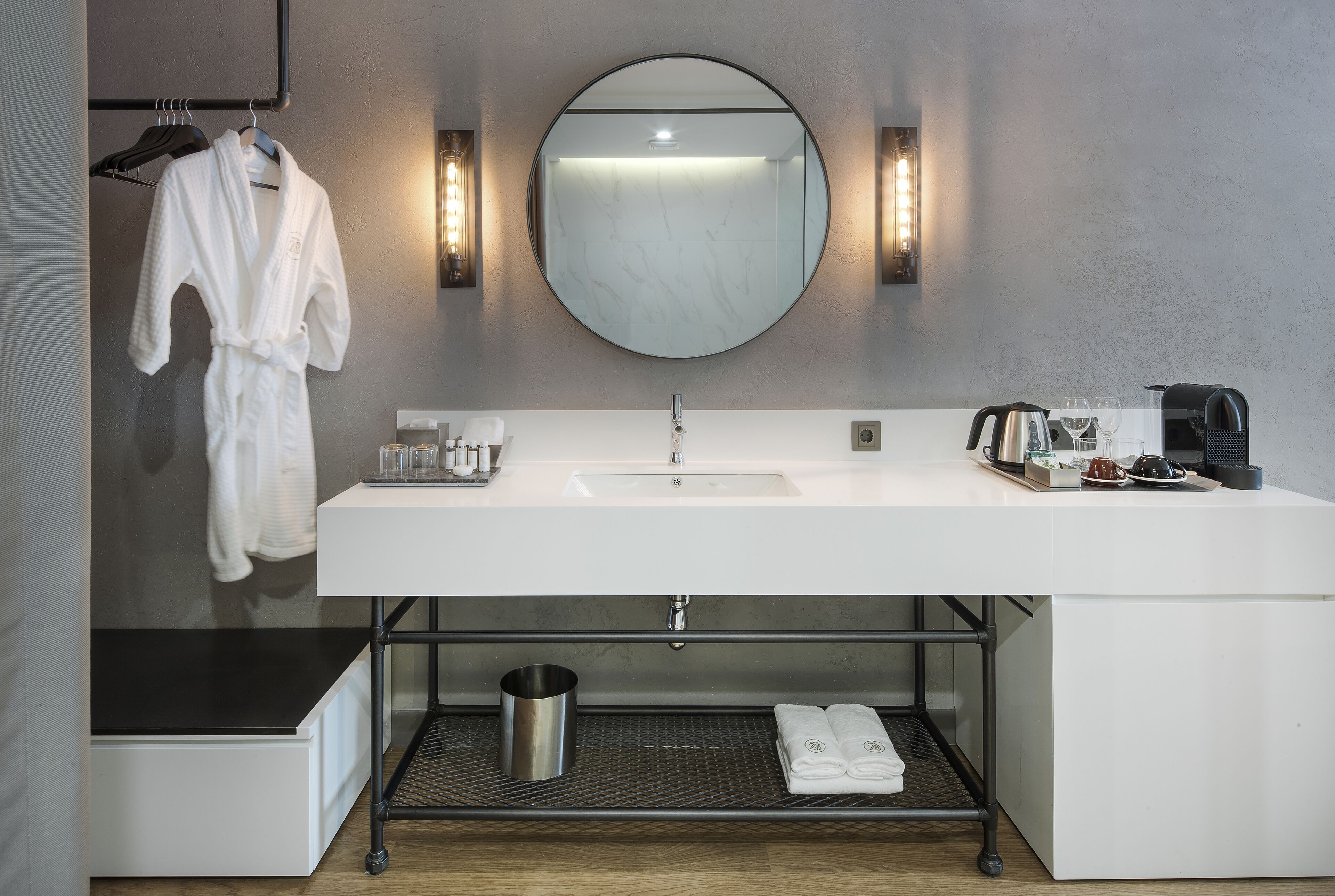 A modern bathroom with a white sink, round mirror, and towel rack.