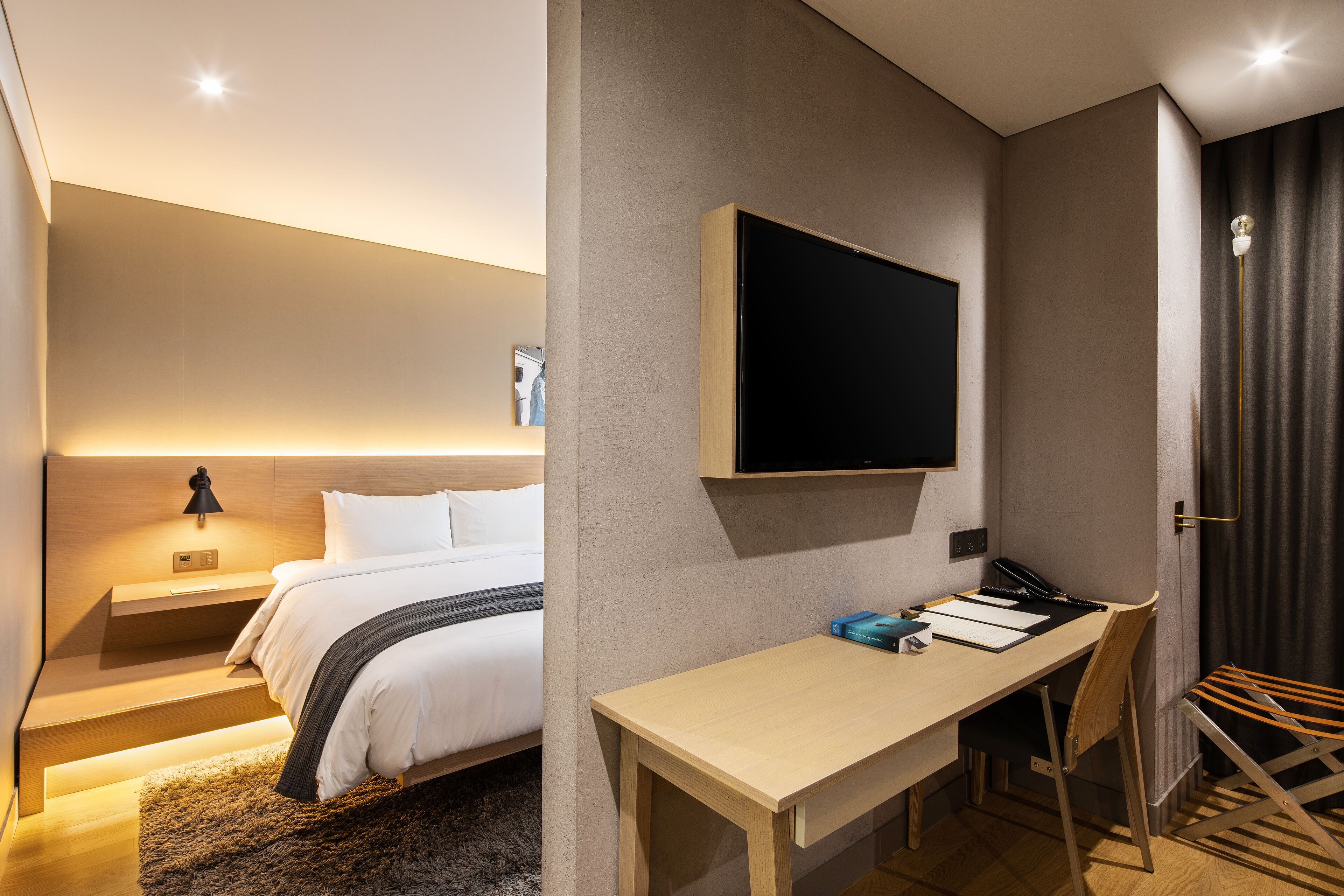 Una habitación de hotel moderna con cama, mesita de noche, escritorio, silla y televisor montado.