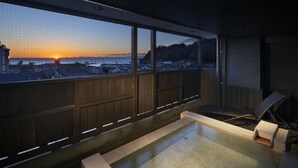 Une terrasse sur le toit offrant une vue sur le coucher de soleil sur la mer, avec des rampes en bois et un jacuzzi.