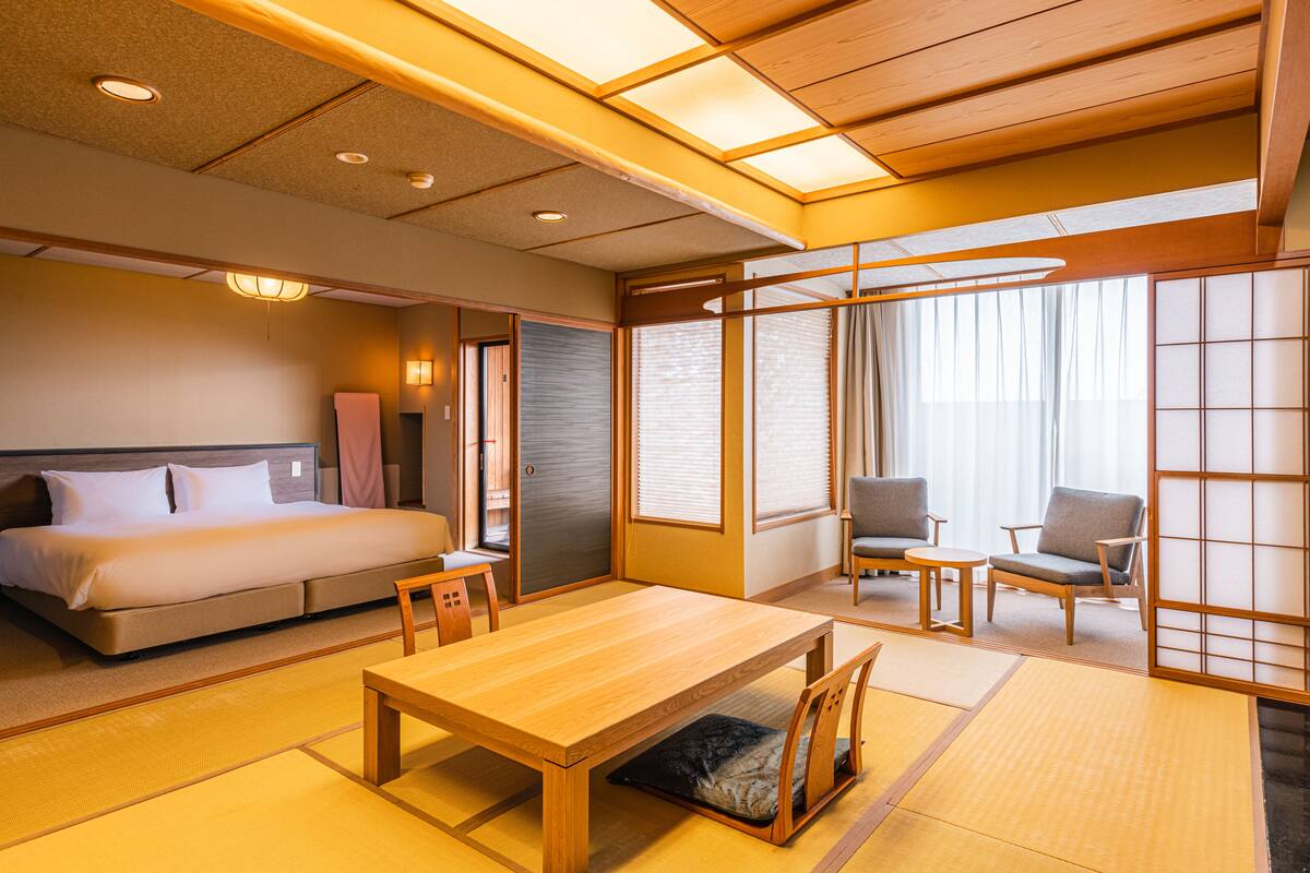 Una habitación tradicional japonesa con suelo de tatami, una mesa de madera baja, una cama con almohada y dos sillas.