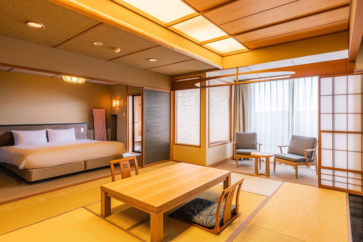 Una habitación japonesa tradicional con suelo de tatami, una cama, una mesa de madera y dos sillas.