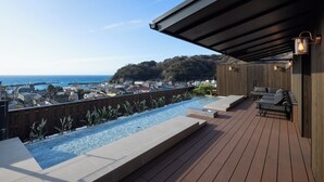 Une piscine sur le toit, dotée d’une terrasse en bois, d’un espace détente avec des coussins et offrant une vue sur l’océan et les collines.