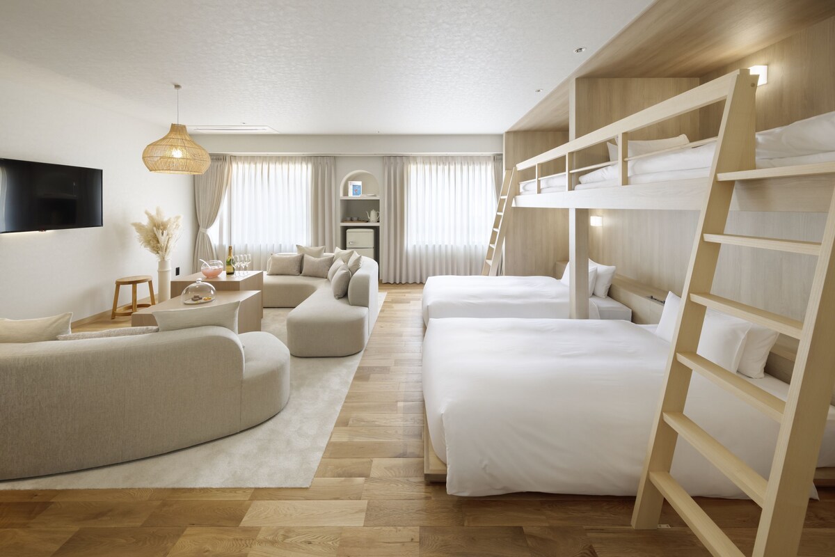 Ein modernes Hotelzimmer mit Stockbetten, einer Schlafcouch, einem Fernseher und einem Schreibtisch.