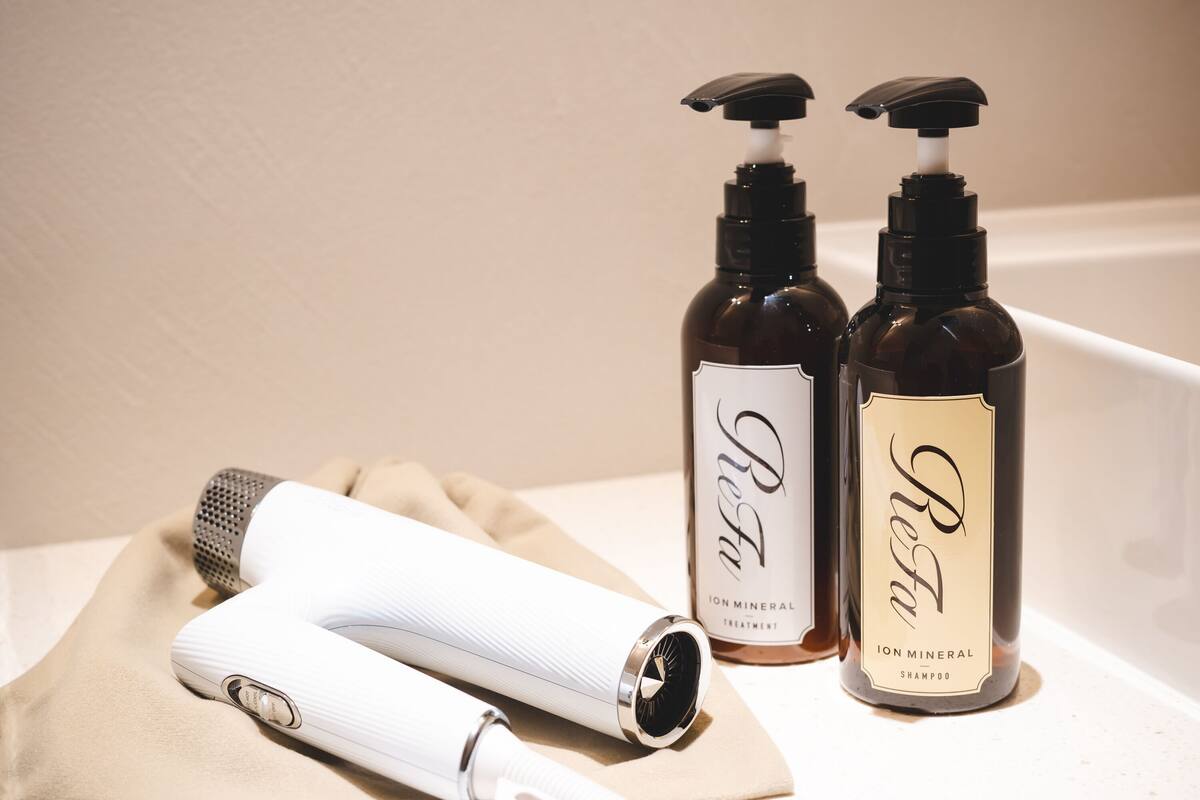 Un baño con una toalla blanca, un secador blanco y dos botellas de productos para el cabello.