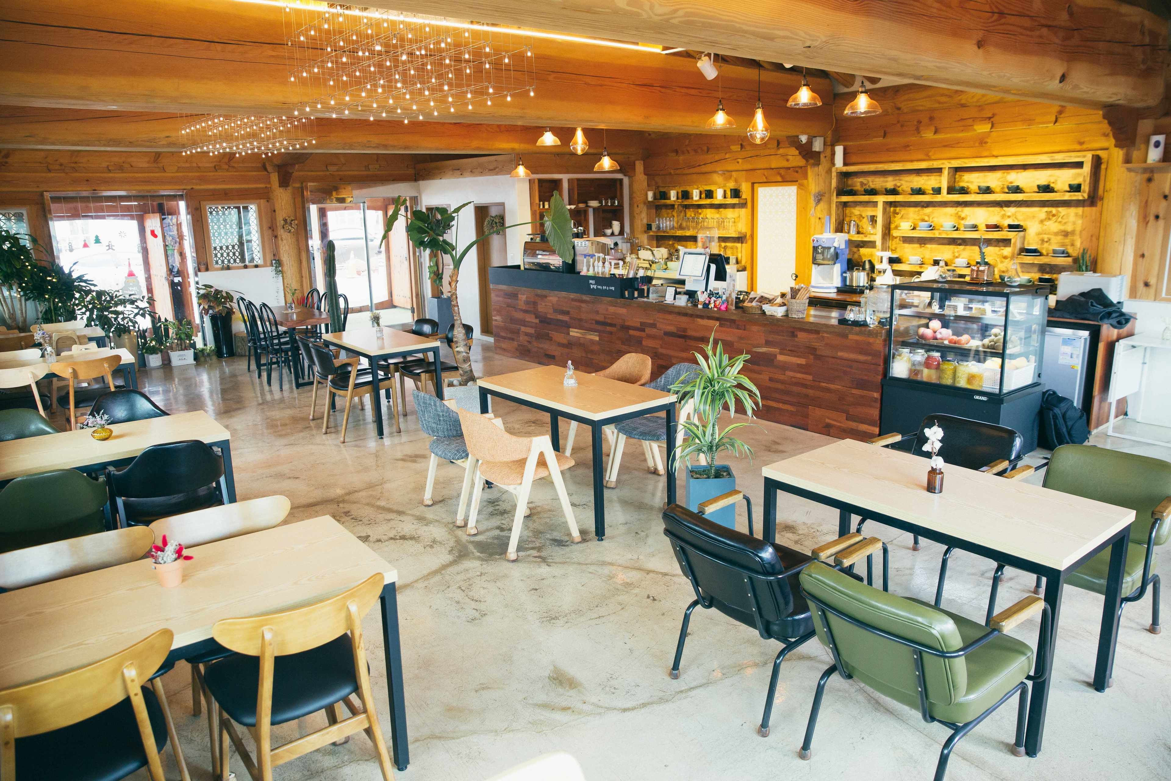 A cozy cafe with wooden interiors, tables, chairs, and a counter with a display case.