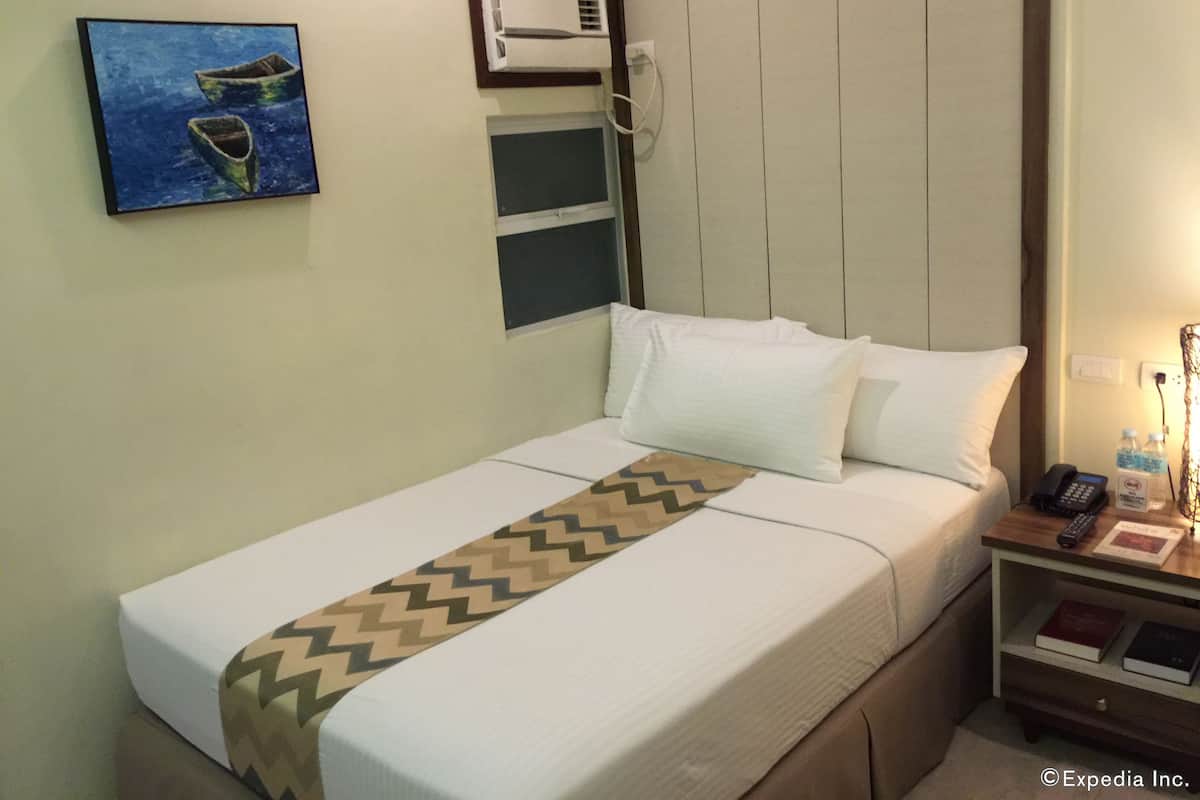Quarto de hotel com cama, pintura de barcos, aparelho de ar condicionado, mesa de cabeceira com telefone e garrafa de água.