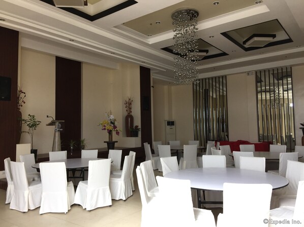 Un'ampia sala da pranzo con tavoli rotondi e sedie bianche, un lampadario decorativo e un grande specchio a parete.