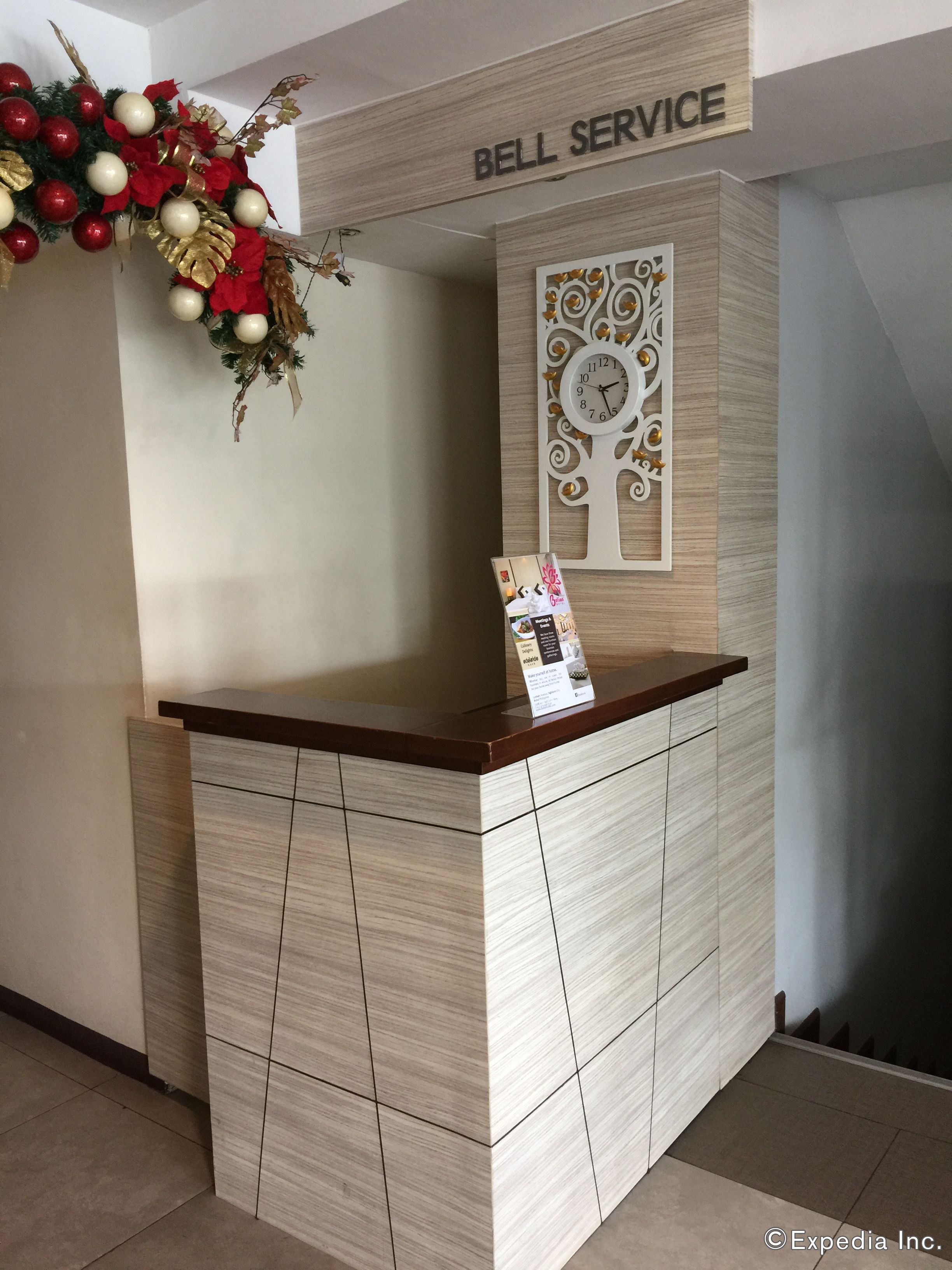 A reception desk with a wooden top and light wood paneling, a wall clock, and a sign reading "Bell Service".