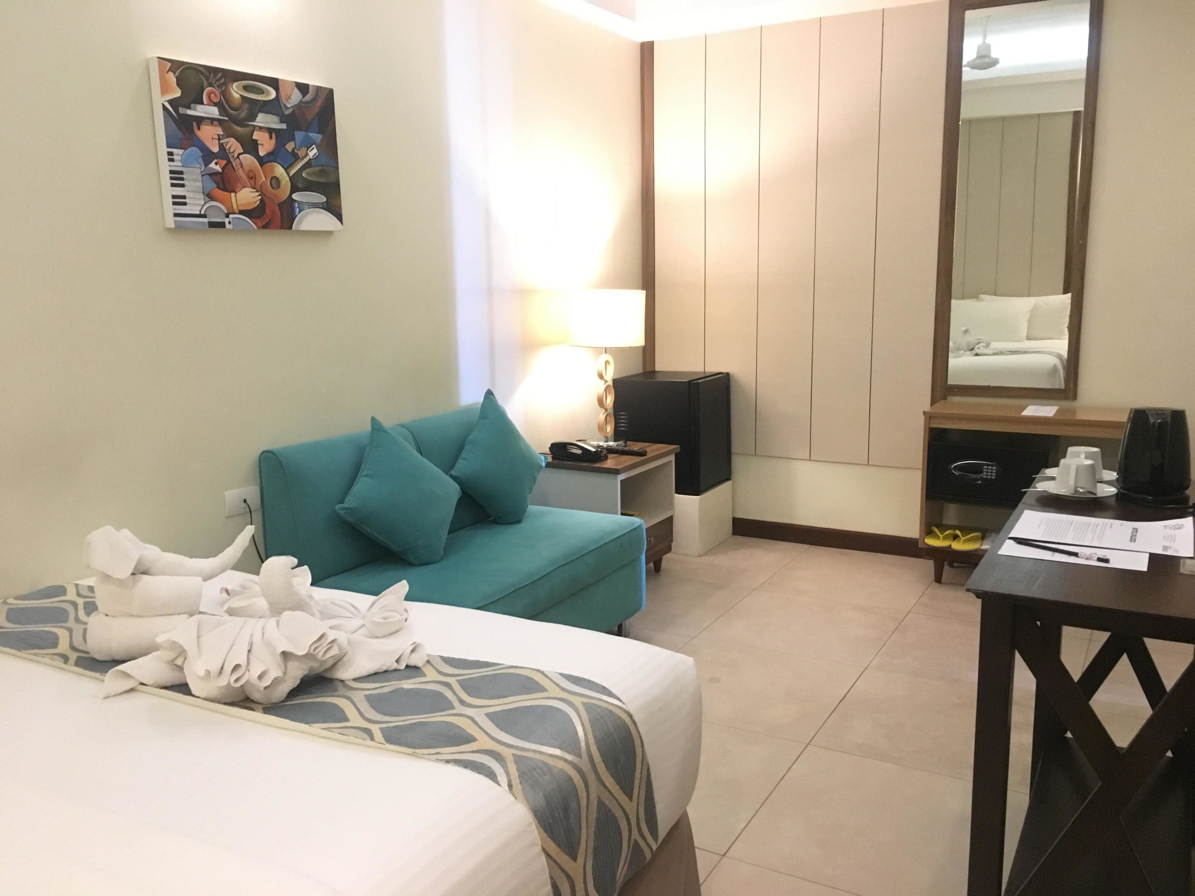 Een hotelkamer met een bed, een slaapbank, een bureau, een lamp, een televisie, een spiegel en een schilderij aan de muur.