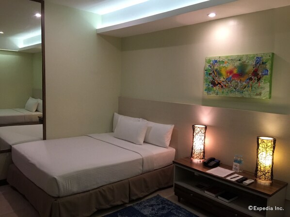 A hotel room with a bed, bedside table, lamp, and artwork on the wall.