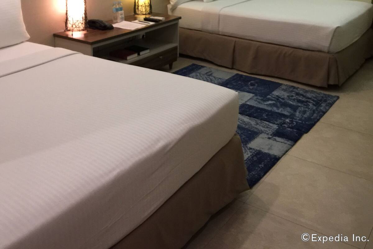 Quarto de hotel com duas camas, uma escrivaninha, uma mesa de cabeceira e um quadro abstrato colorido na parede.