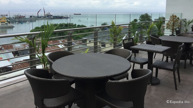 A balcony with wicker furniture overlooking a harbor with boats and a crane. - Belian Hotel (Tagbilaran)