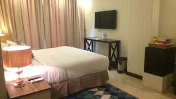 Habitación de hotel con cama, escritorio con lámpara, televisor en la pared y un cubo de basura.