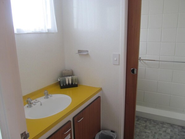 A bathroom with a yellow sink, a mirror, a towel rack, and a small trash bin. - Parkview Motel (Dargaville)