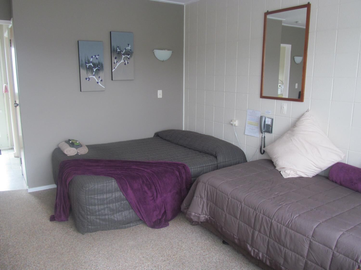 A bedroom with two beds, a bedside table, a wall-mounted phone, and two wall-mounted paintings.