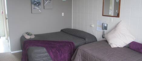 A bedroom with two beds, a bedside table, a wall-mounted phone, and two wall-mounted paintings.