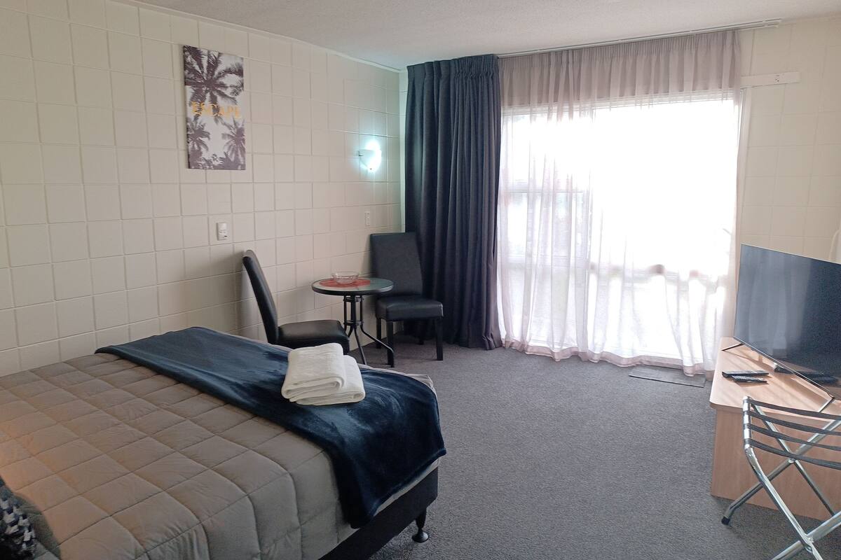 A hotel room with a bed, a desk, a chair, a television, and a window with curtains.