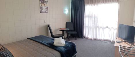 Habitación de hotel con cama, escritorio, silla, televisión y ventana con cortinas.