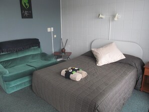 A bedroom with a bed, a green sofa, a small table with a vase, and a wall-mounted light fixture. - Parkview Motel (Dargaville)