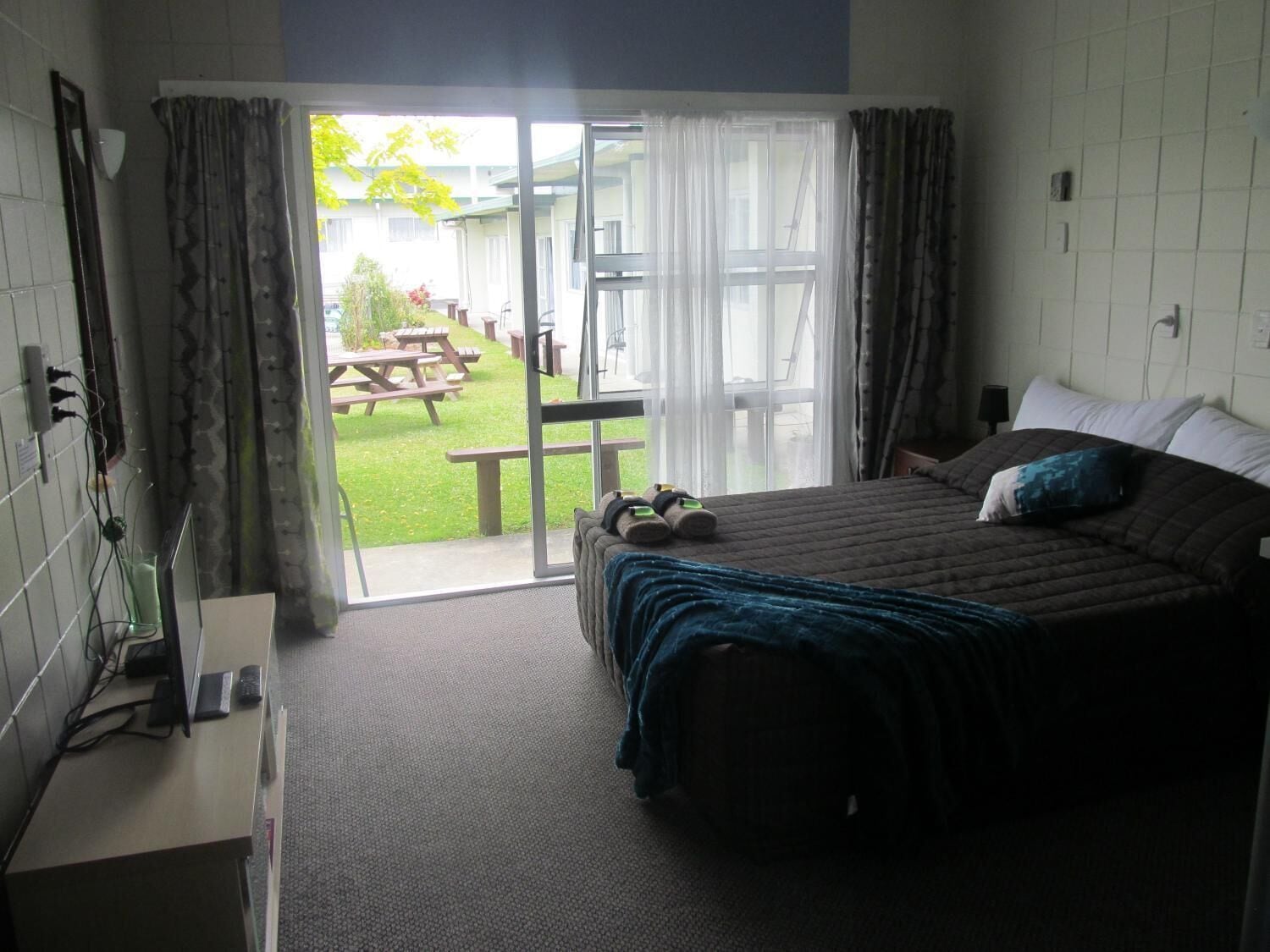 Ein Schlafzimmer mit einem Bett, einem Schreibtisch mit Computer und Blick auf eine Terrasse mit Tisch und Stühlen.