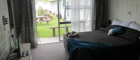 Ein Schlafzimmer mit einem Bett, einem Schreibtisch mit Computer und Blick auf eine Terrasse mit Tisch und Stühlen.