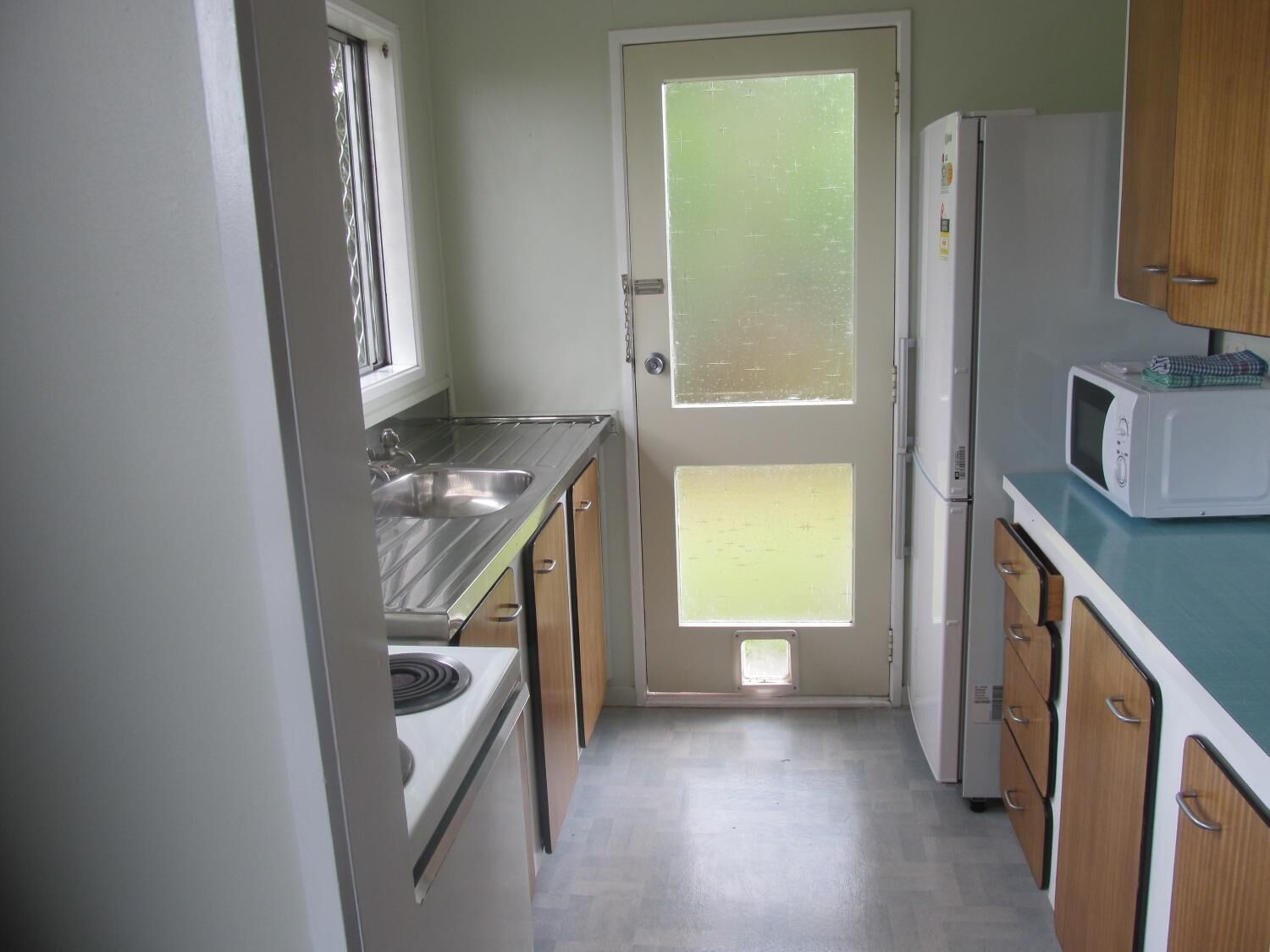 Una cocina compacta con pileta, cocina, horno microondas y alacenas de madera.